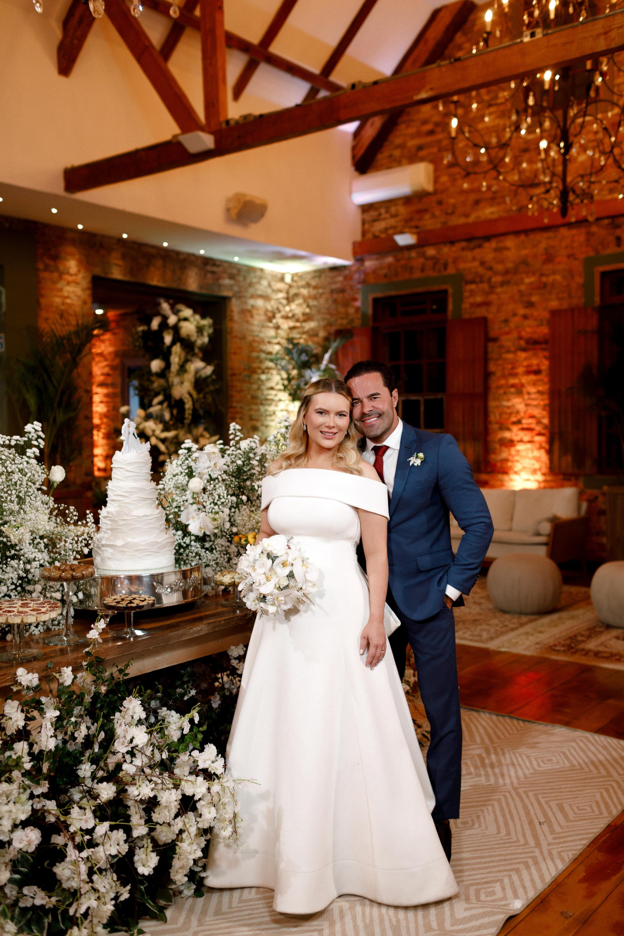Adriana e Nilsen junto ao bolo e aos arranjos de flores